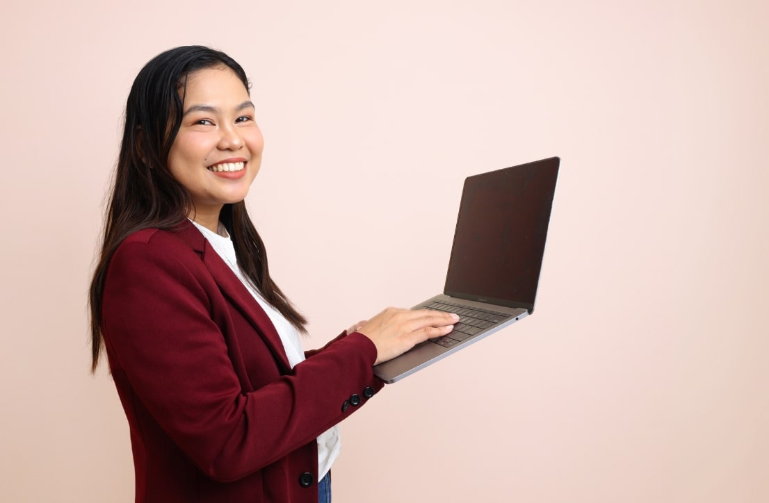 Roma, a freelance web designer and developer in a burgundy blazer, smiling while typing on an open laptop.
